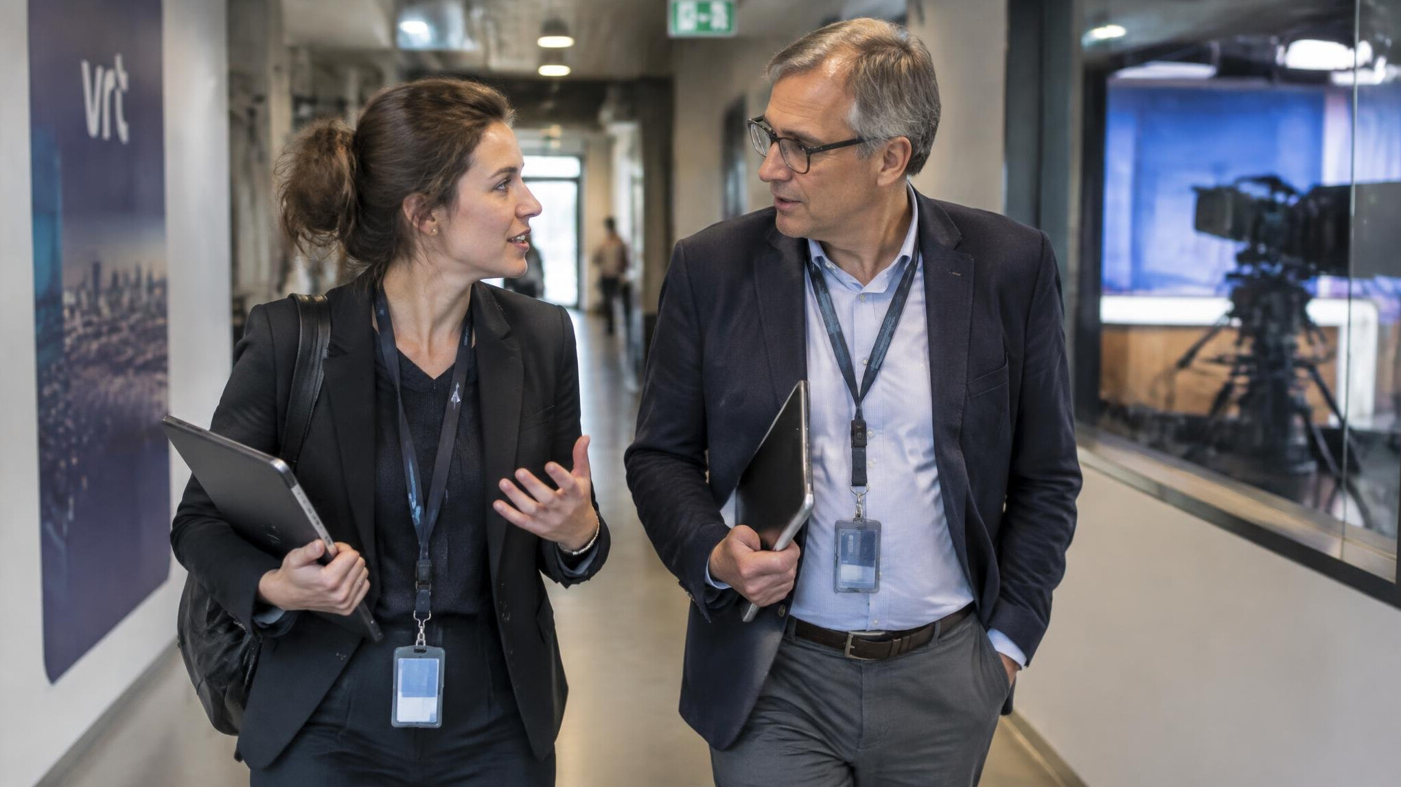 Twee collega's overleggen kort in de gang van een televisiestudio